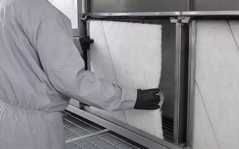 Tecnico della manutenzione durante la sostituzione dei pannelli filtranti paint arrestor in fibra di vetro in una cabina di verniciatura.
