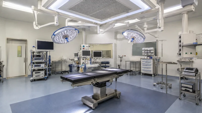 Sala operatoria ospedaliera con tavolo chirurgico, lampade scialitiche e sistema di ventilazione a soffitto.